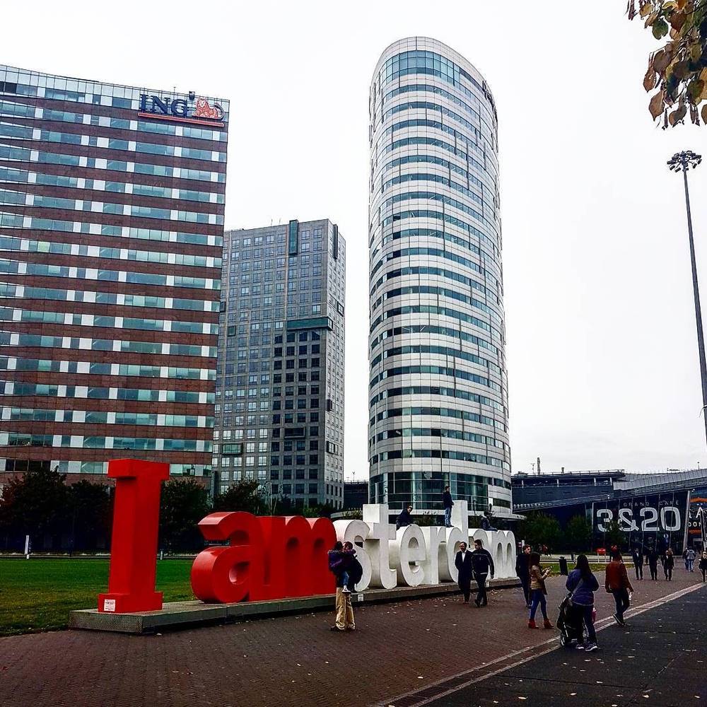 The "I amsterdam" letters sculpture on a plaza with office towers behind it.