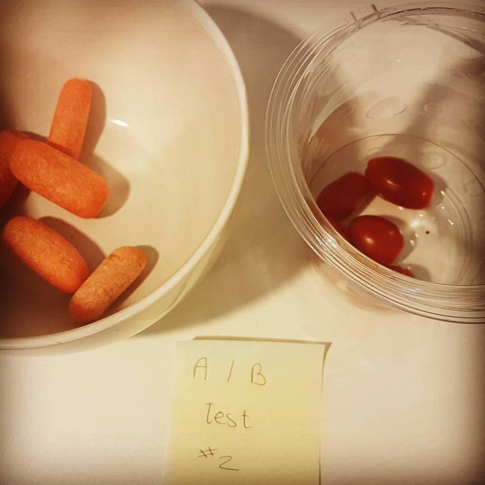 Two bowls of carrots and cherry tomatoes on a counter with a note reading "A/B test #2".