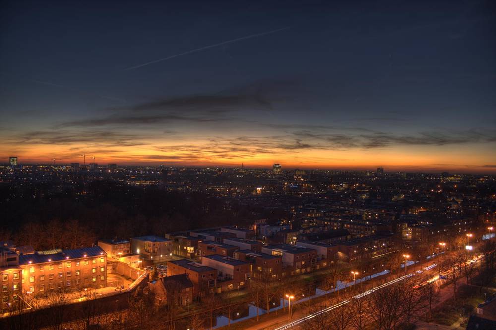 A city skyline glows orange at dusk in an HDR panorama, lights coming on below.