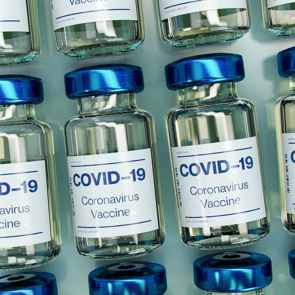 Rows of glass vials labeled COVID-19 Coronavirus Vaccine with blue caps.