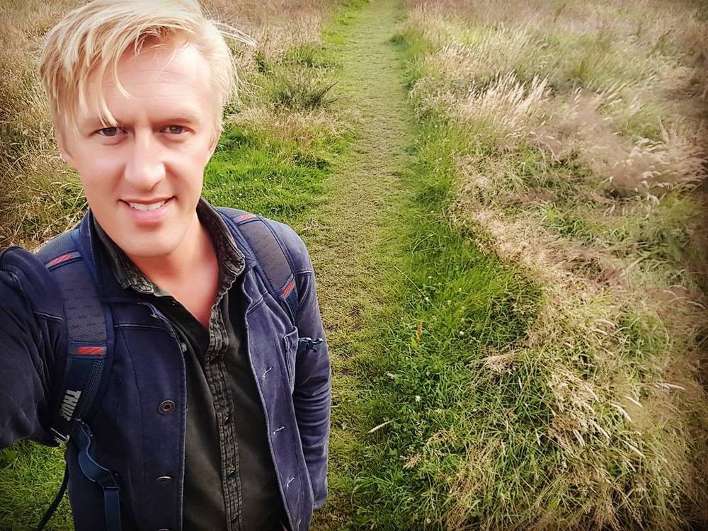 Selfie of a man standing on a grassy path through tall reeds.