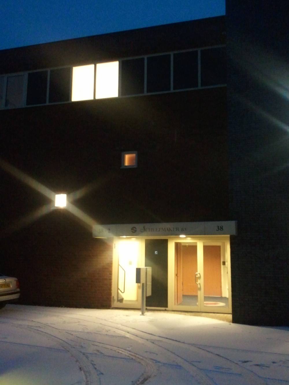 A lit office building entrance glows against the twilight sky above a snowy path.