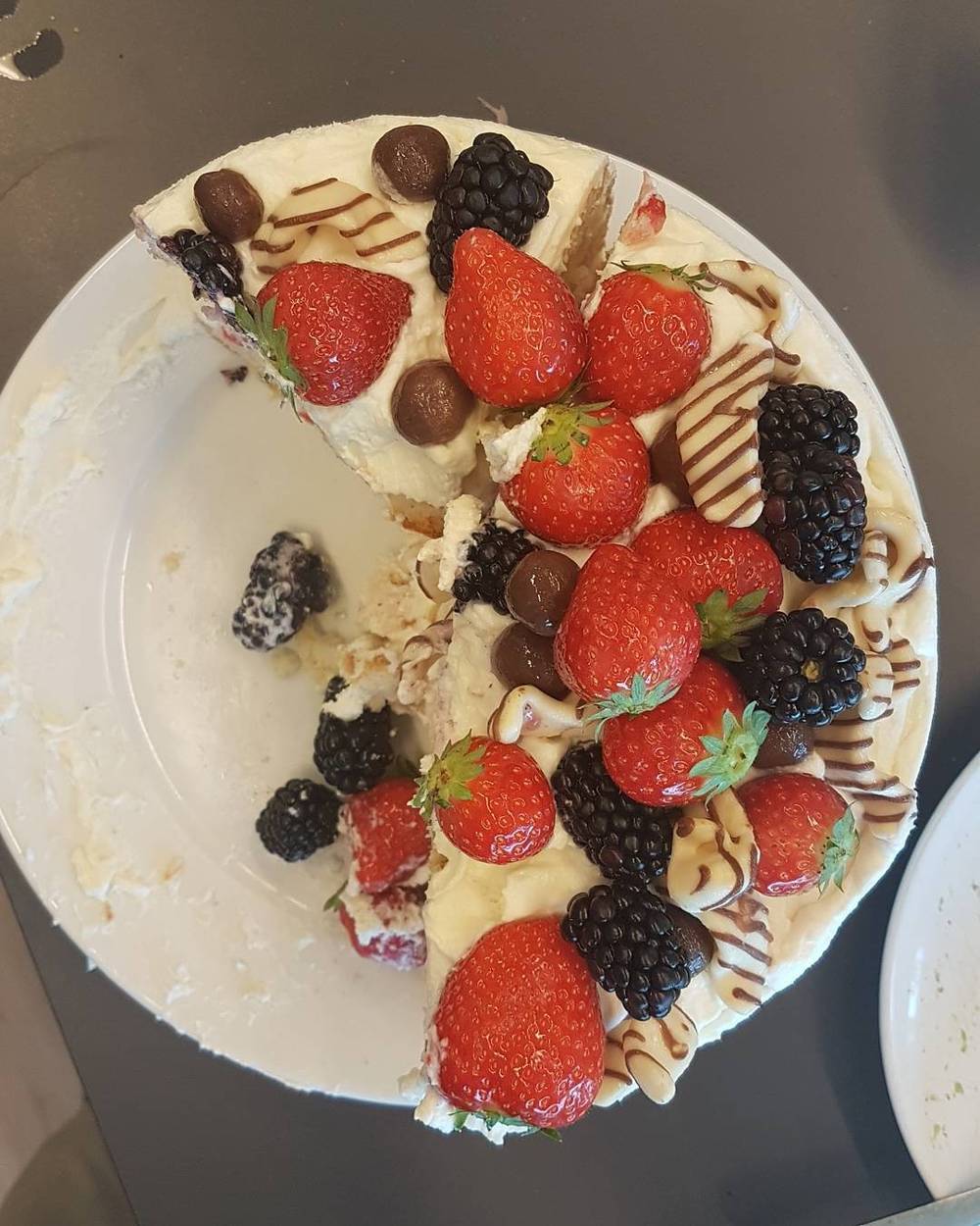 A slice of cake topped with strawberries, blackberries and chocolate drizzle on a plate.