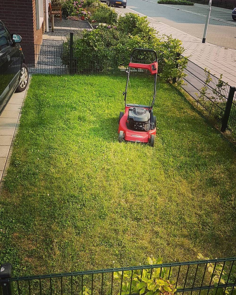 A red lawnmower sitting on a neatly trimmed lawn behind a fence.