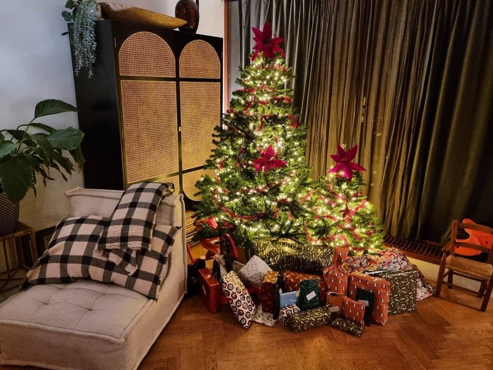 A living room with a lit and decorated Christmas tree surrounded by wrapped presents.