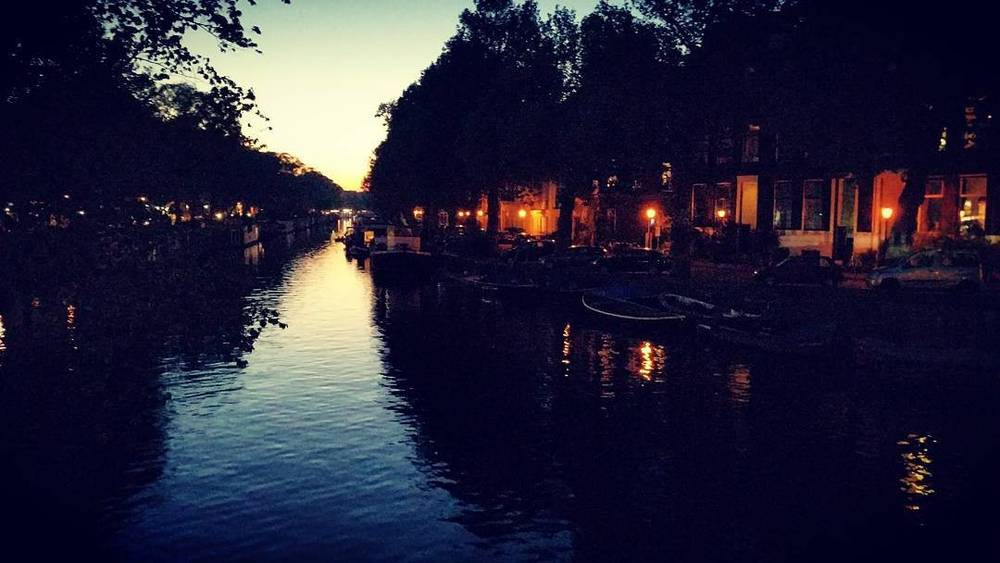 A canal in Amsterdam at dusk, lined with boats and glowing streetlights.