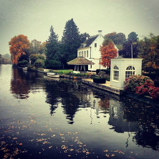 A white waterside house with autumn trees reflected in a canal.