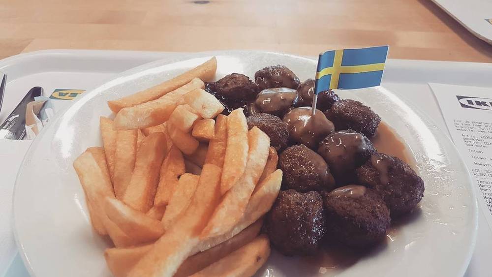 A plate of Swedish meatballs and french fries with a small Swedish flag stuck in the food.
