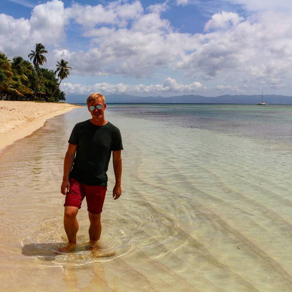 A man standing in shallow, clear turquoise water on a tropical beach.