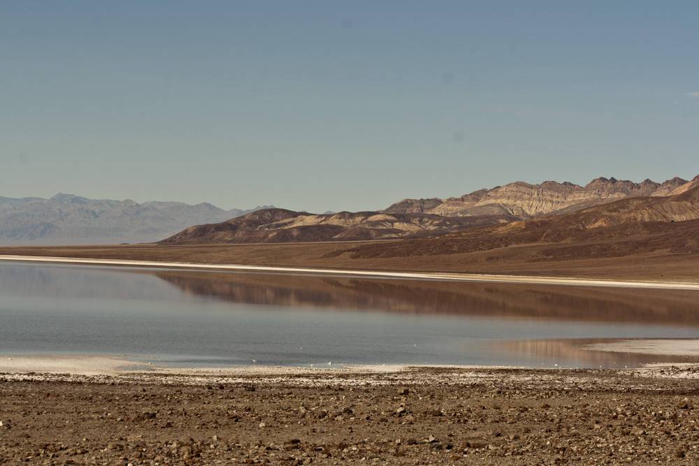 A calm, reflective salt lake mirrors the surrounding desert mountains.