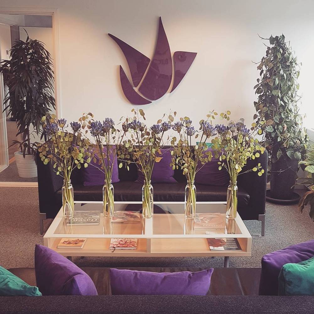 A hotel lobby with a purple bird-shaped wall sculpture, purple sofas and vases of dried flowers.