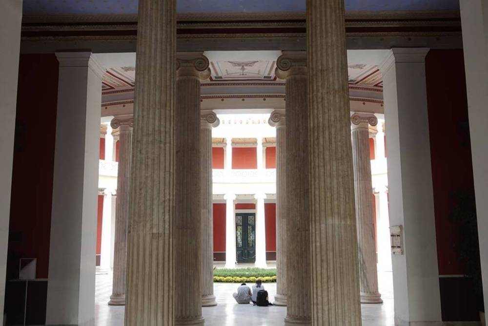 Looking through a row of tall marble columns into a bright interior hall of the Zappeion.