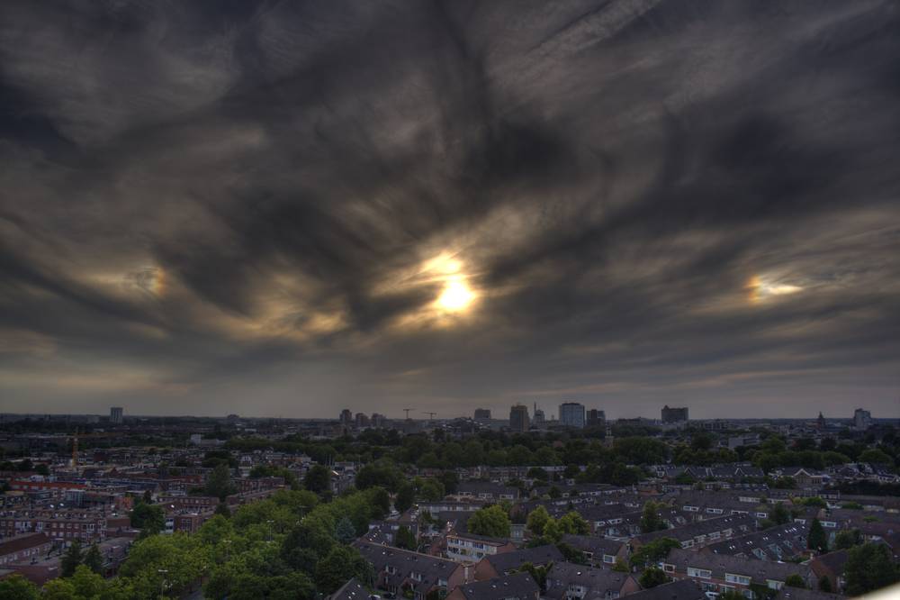 Two bright sun dogs flanking the sun in swirling dark clouds above the Utrecht skyline.