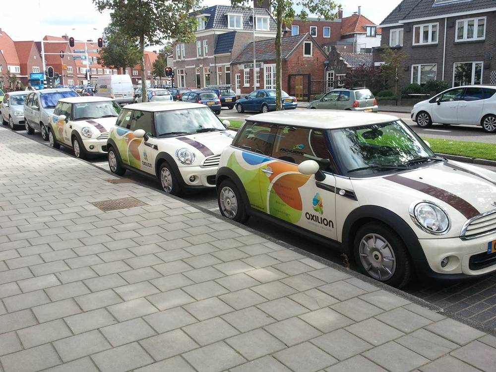 A row of white Mini Coopers with colorful Oxilion branding parked along a street.