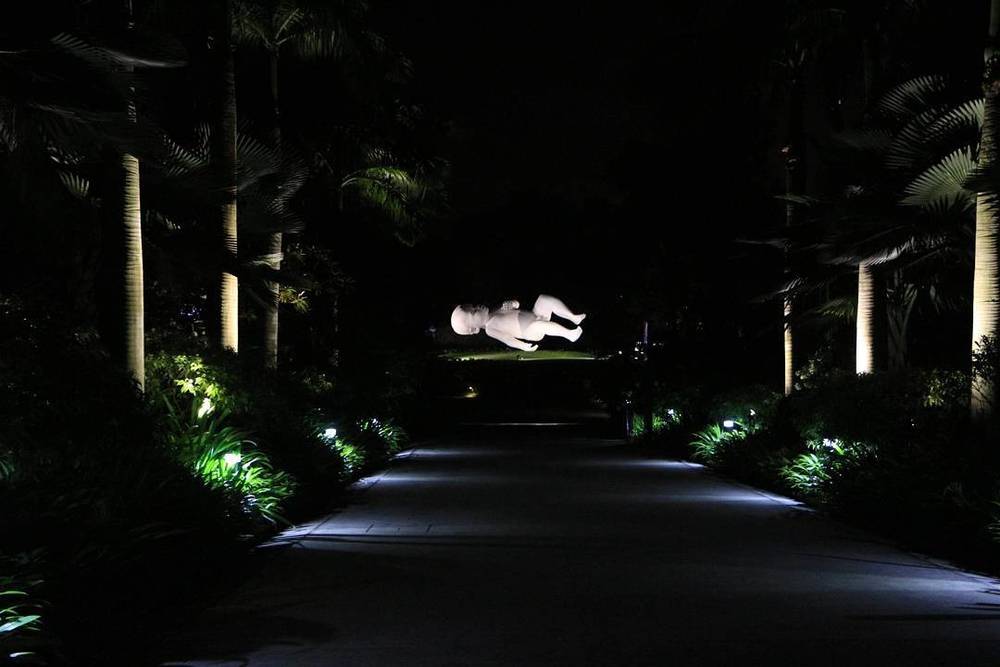 A ghostly white sculpture of a floating figure illuminated along a garden path at night.