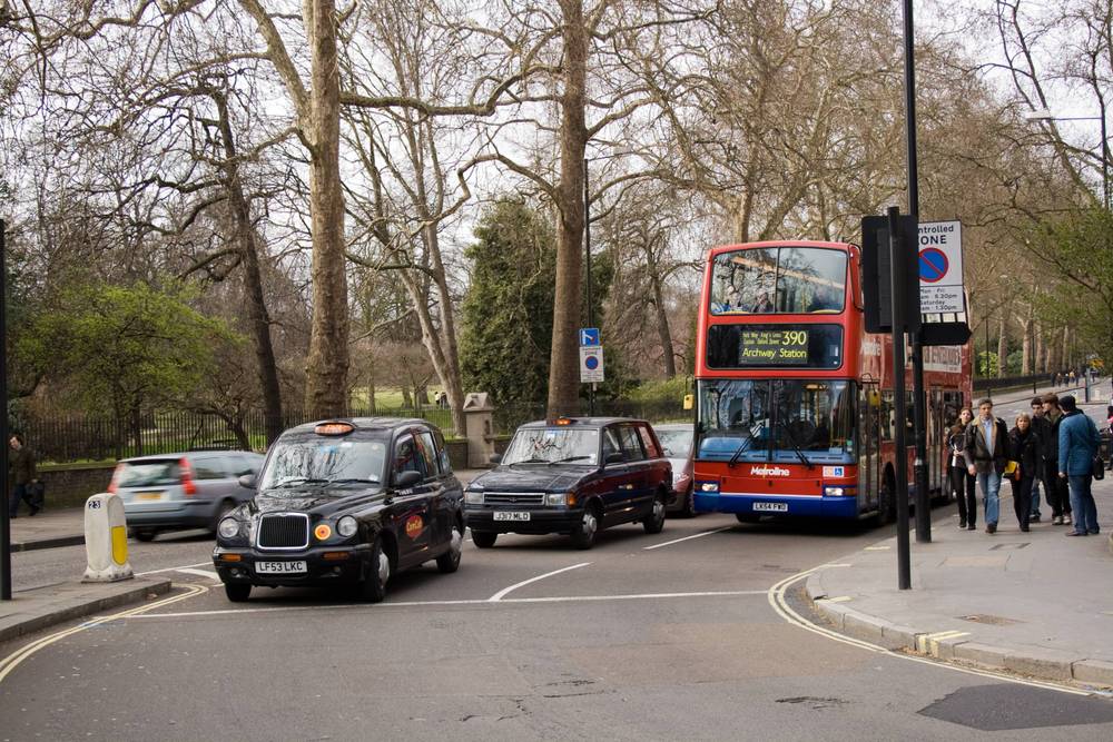 Black cabs and a red double-decker bus wait at a busy London street crossing.