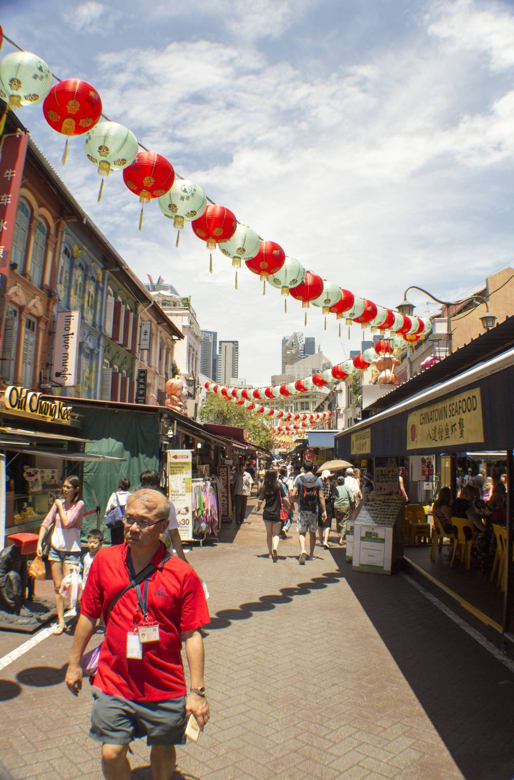 Shoppers walk beneath strings of red and white lanterns along a Chinatown market street.