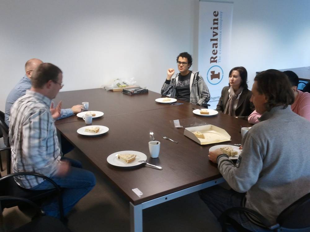 A group gathers around a conference table with coffee and pastries at a 'Realvine' branded meeting.