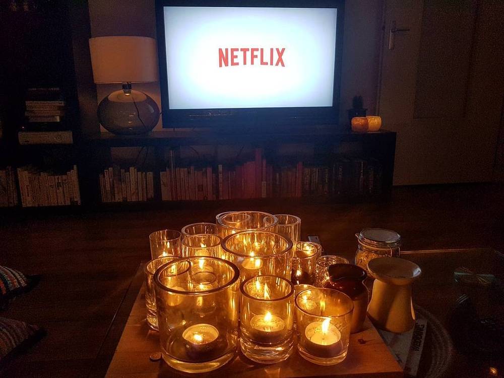 A living room coffee table covered with lit candles, with a television showing Netflix in the background.