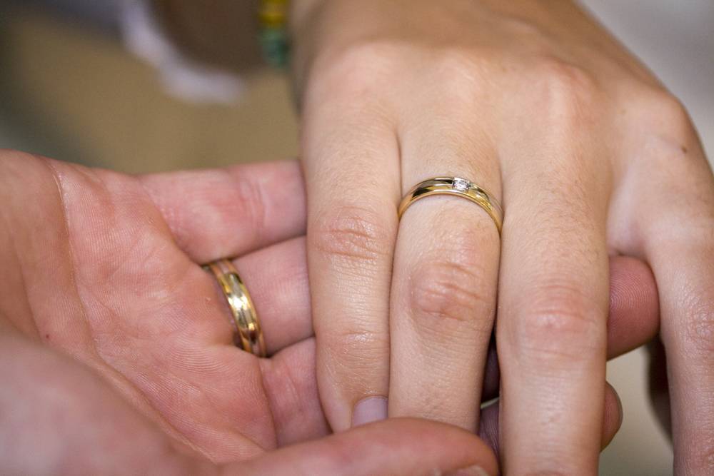 Close-up of two hands, one wearing a wedding ring, clasped together.