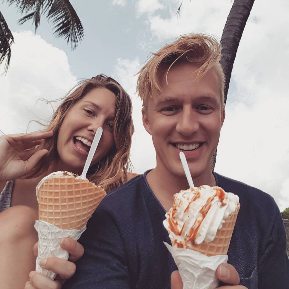 A couple eating ice cream cones and smiling under palm trees.