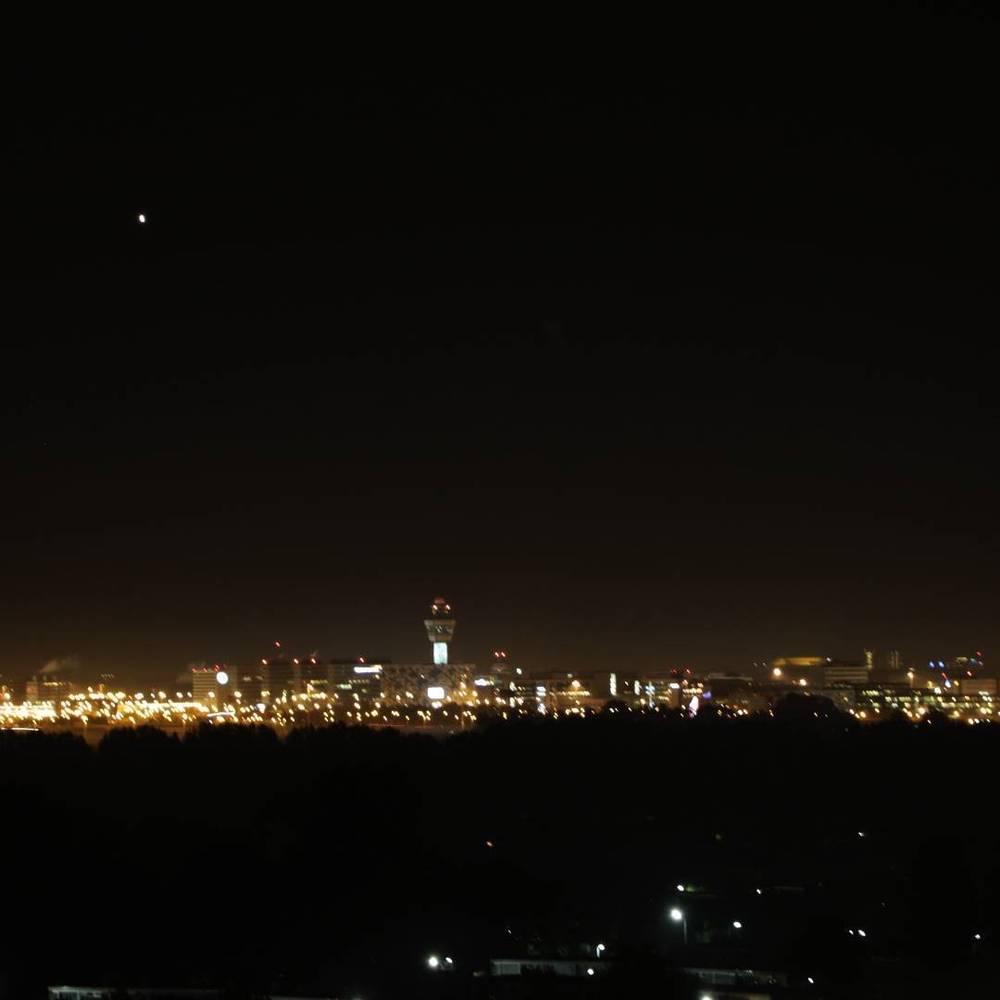 A city skyline and airport control tower lit up at night, seen from a distance.