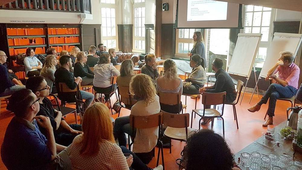 An audience seated in a wood-paneled room listening to a presentation.