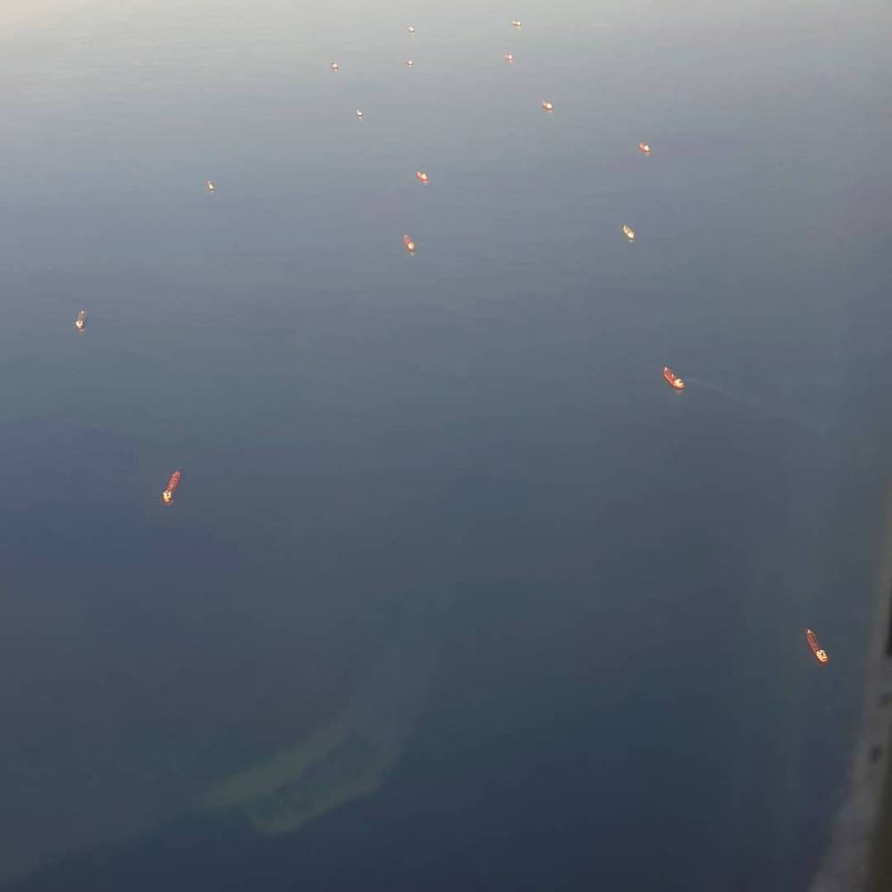 View from an airplane window over water with distant flares, possibly oil platforms, visible.