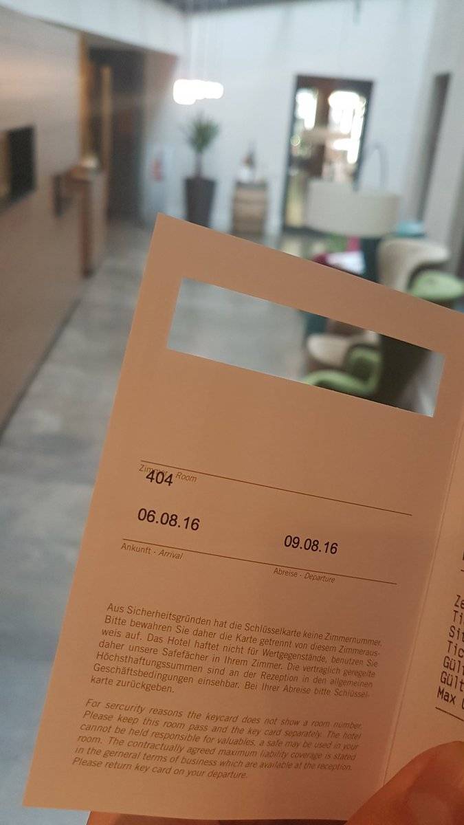 A hand holding a hotel key card sleeve in front of a modern lobby interior, in Leipzig.