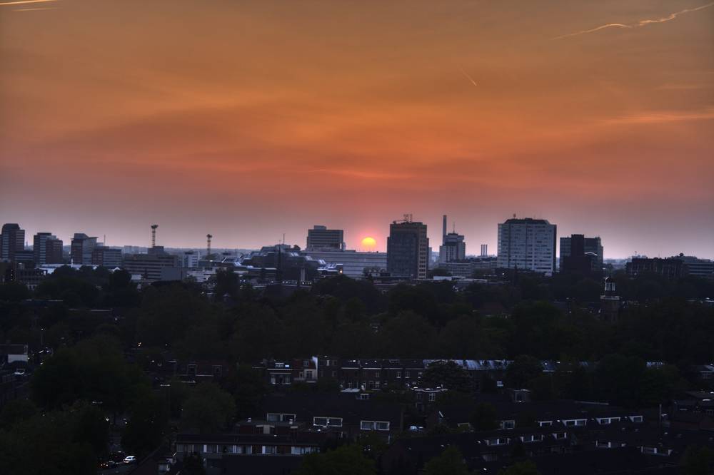The sky glows deep orange at sunset over the Utrecht skyline and rooftops.