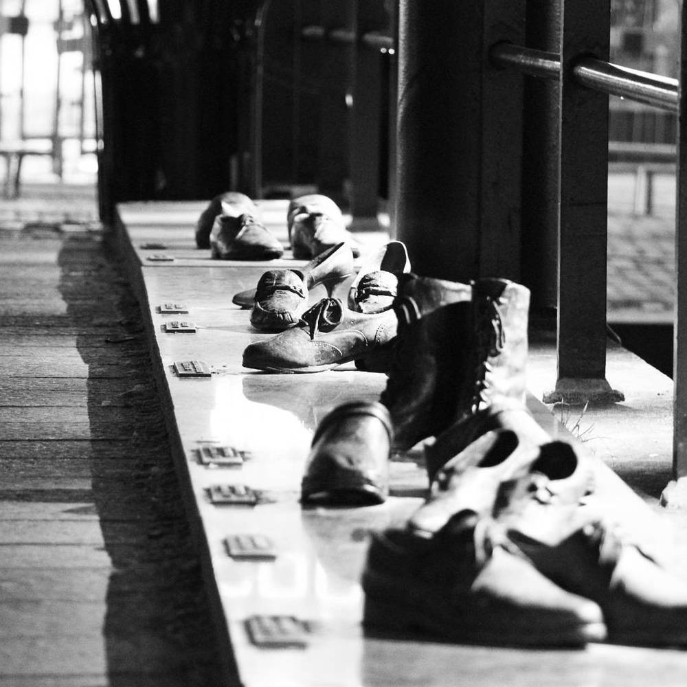A black and white photo of rows of old shoes lined up along a ledge, as part of a memorial display.