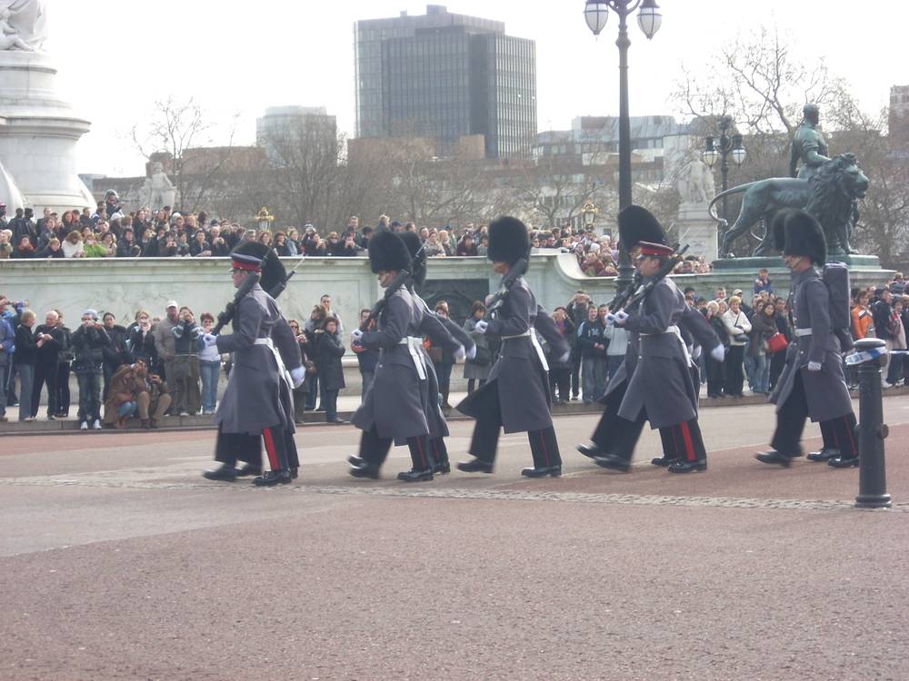 Guardsmen in bearskin hats march past crowds near Buckingham Palace.