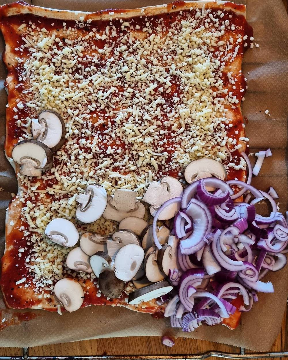 An overhead view of a homemade pizza topped with mushrooms, red onion, and cheese before baking.
