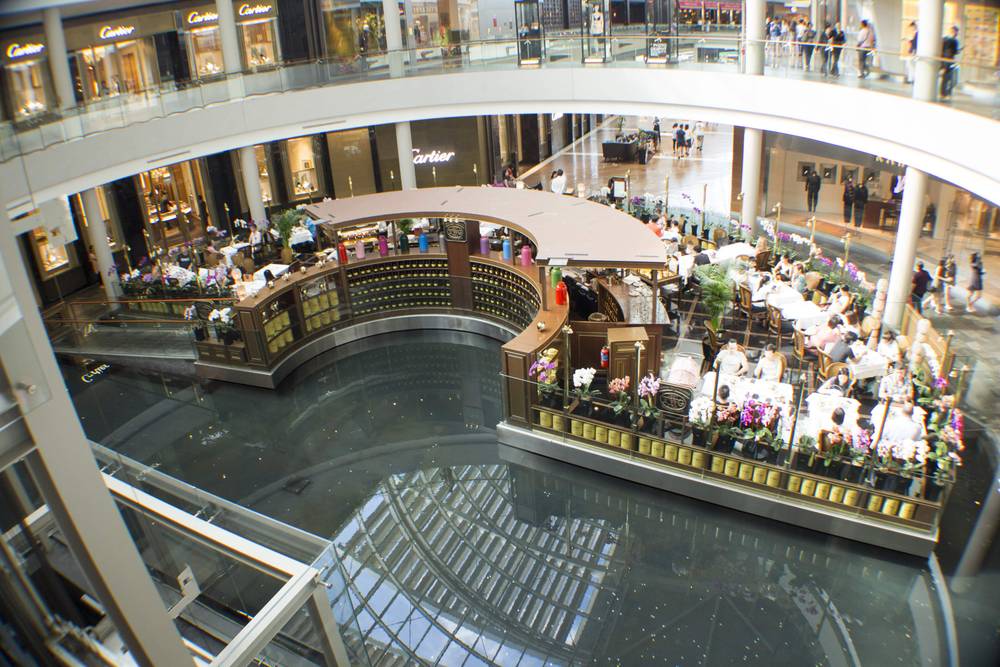 Diners sit at a restaurant terrace beside the indoor canal at the mall.
