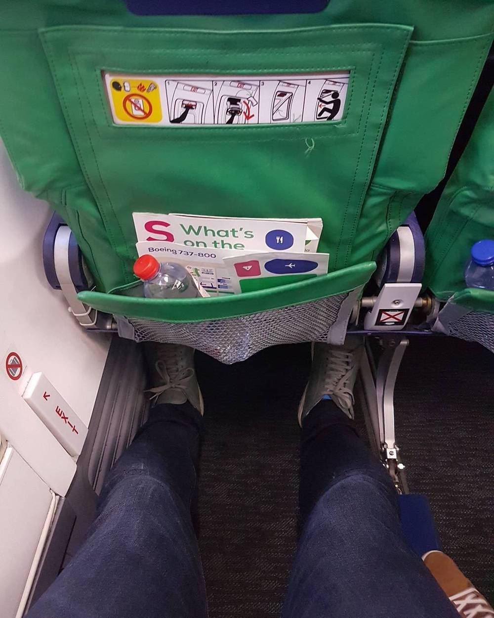 View of legs stretched out in an airplane seat with the seatback safety card visible.