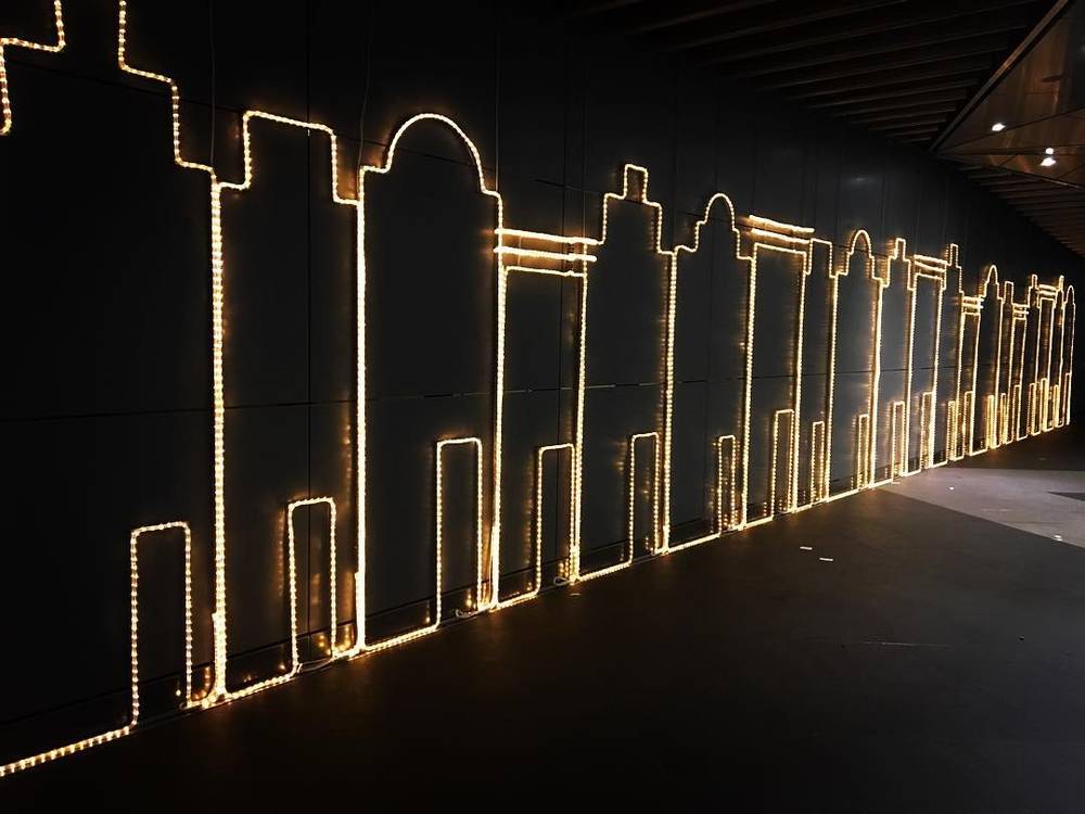 An illuminated outline drawing of a city skyline made from string lights on a dark wall.