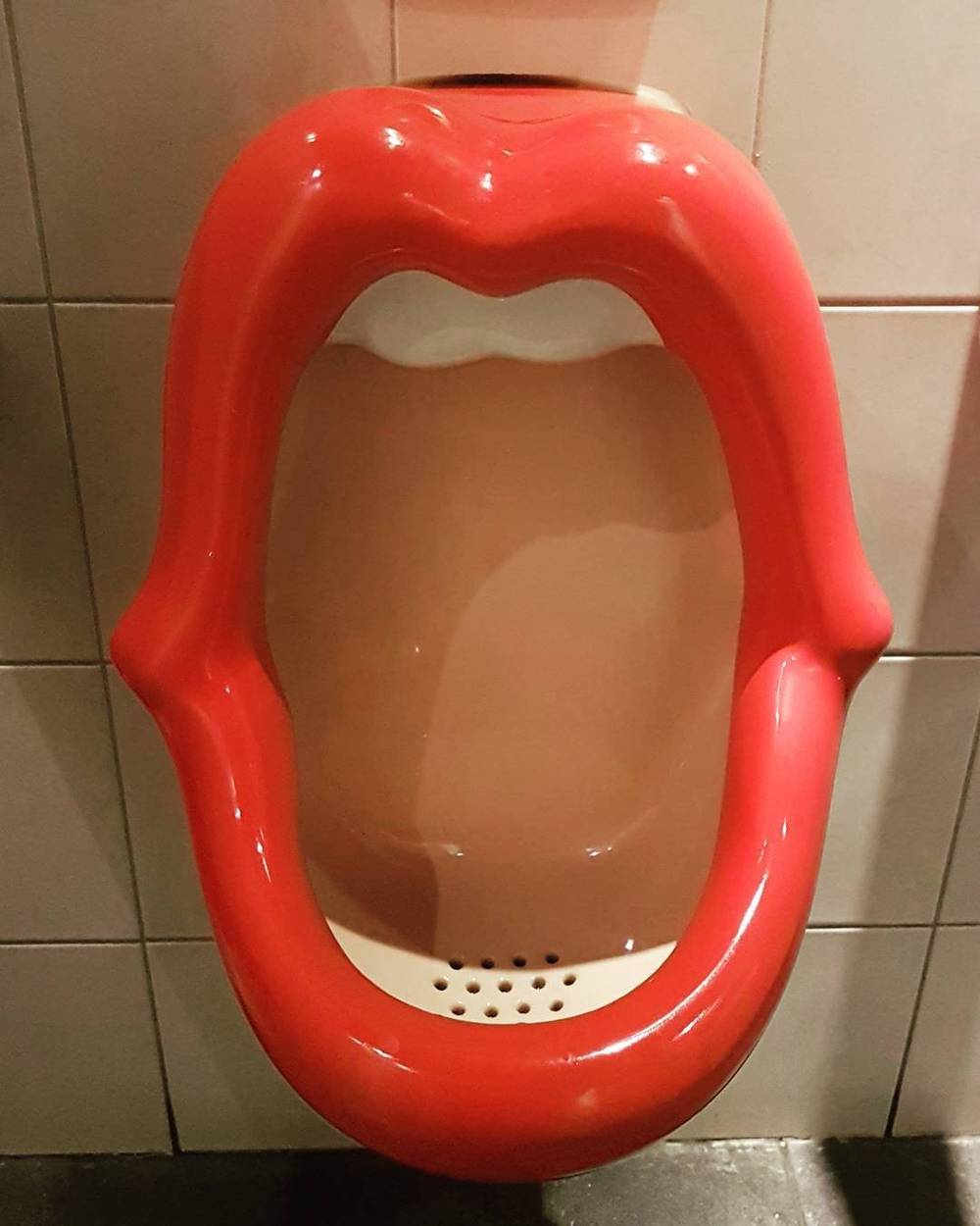 A red urinal shaped like an open mouth mounted on a tiled wall.