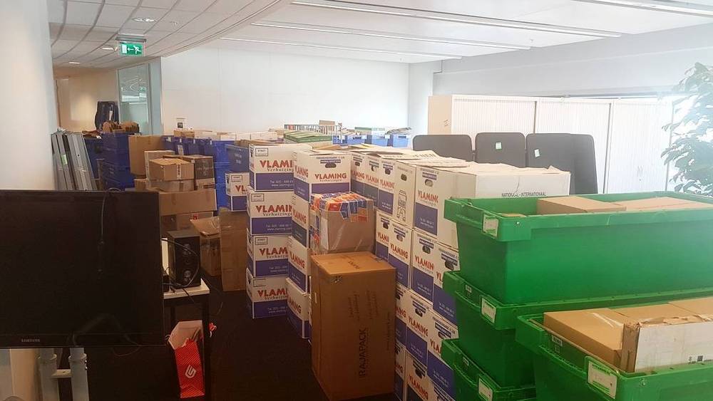 Stacks of moving boxes and green crates filling an office being packed up for a move.