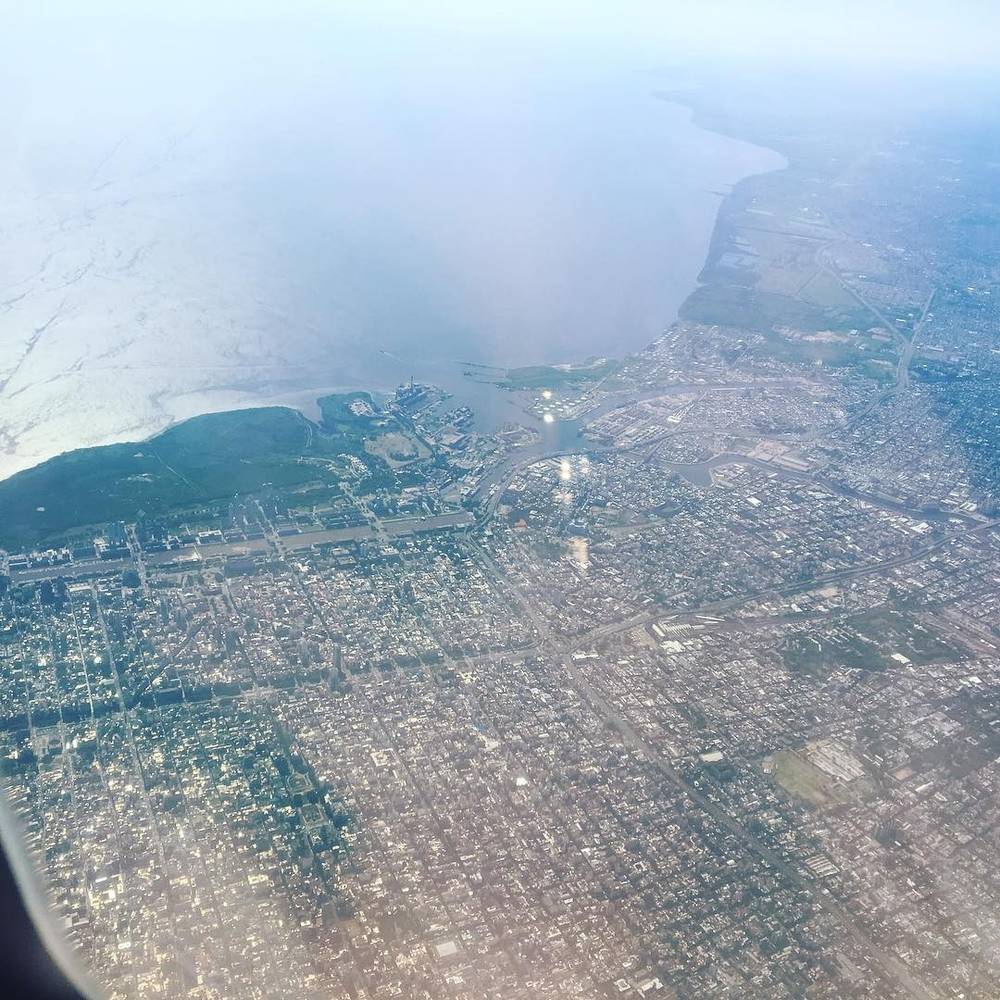 An aerial view of Buenos Aires from an airplane window, showing the coastline and city grid.