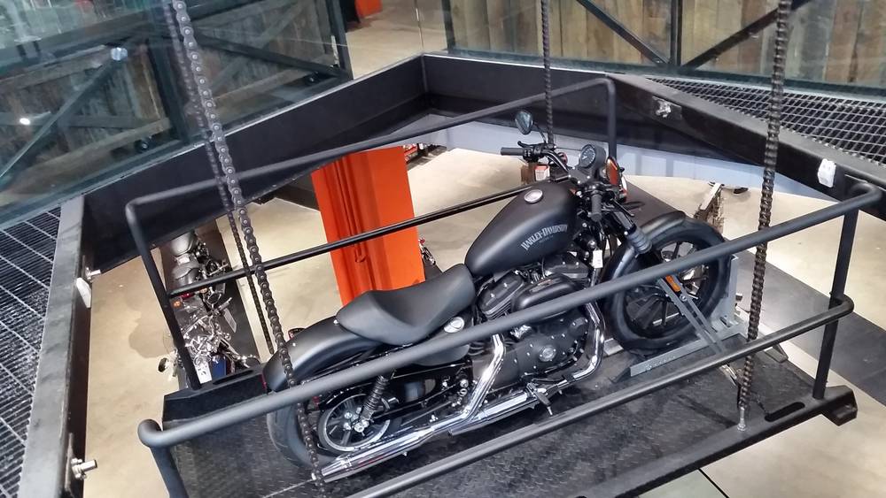 A Harley-Davidson motorcycle sits on a raised display cage inside a multi-level showroom.