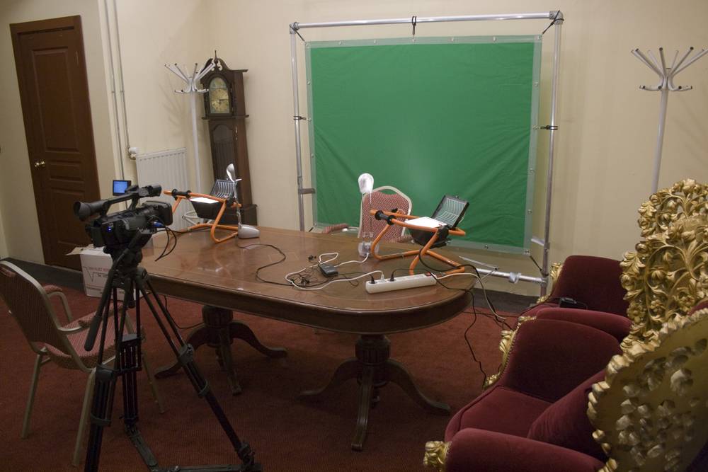 A green screen video setup with camera and lights arranged around an antique table in a historic room.