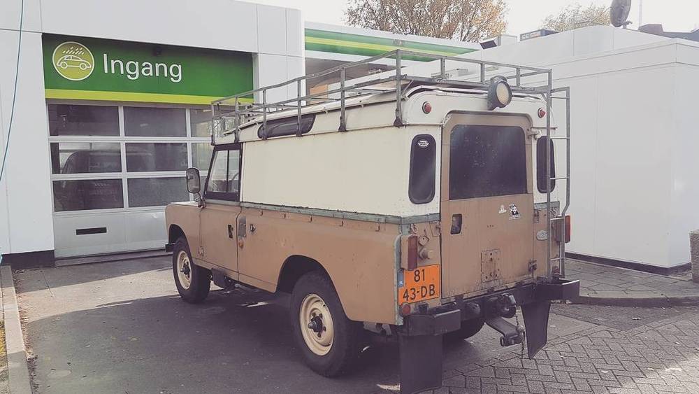 A vintage Land Rover camper conversion parked outside a garage.