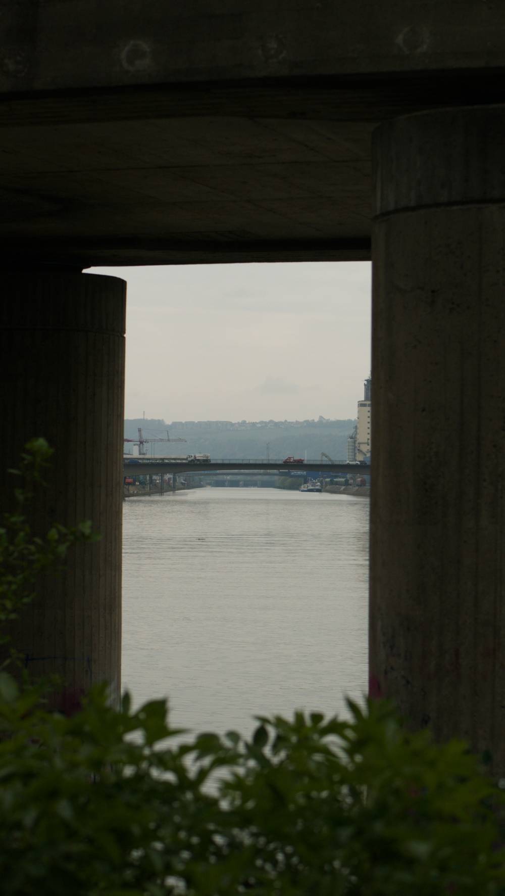 view framed by concrete bridge, pillars and a bush on the bottom;
view following the Neckar south, freight harbor in the distance