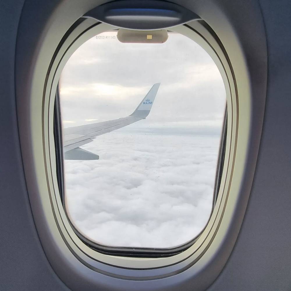 View through an airplane window of the wing above a sea of clouds.