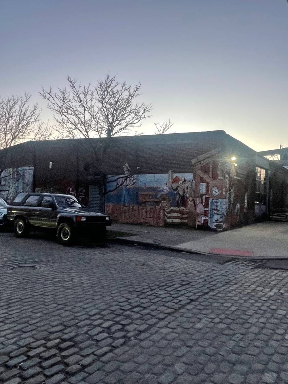 mural of grain cultivation and distillery on corner of brick warehouse with an off road suv in front