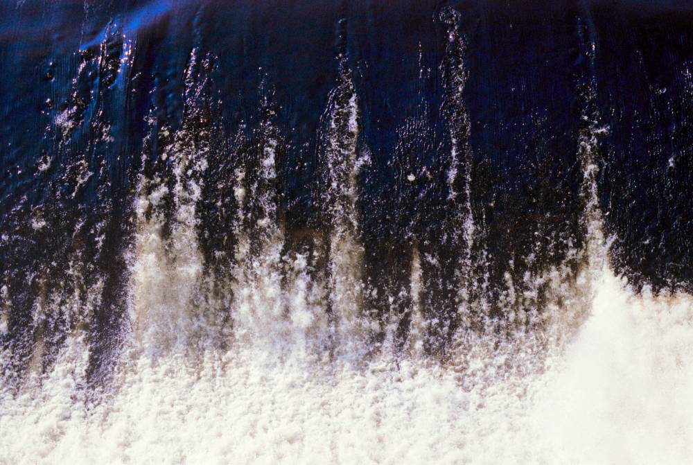 Dark blue water cascades downward, turning into white foam and spray as it crashes against an unseen surface.