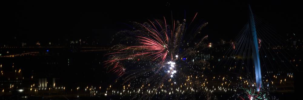 Fireworks exploding above illuminated bridges over the water.