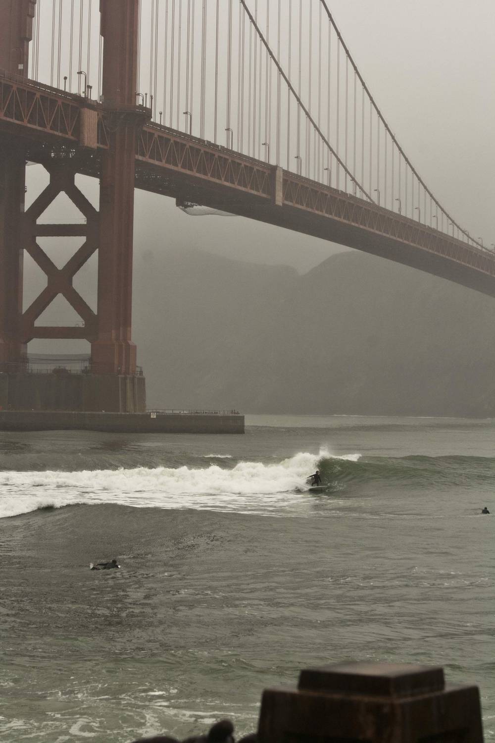 Surfers wait for waves beneath the fog-shrouded Golden Gate Bridge.