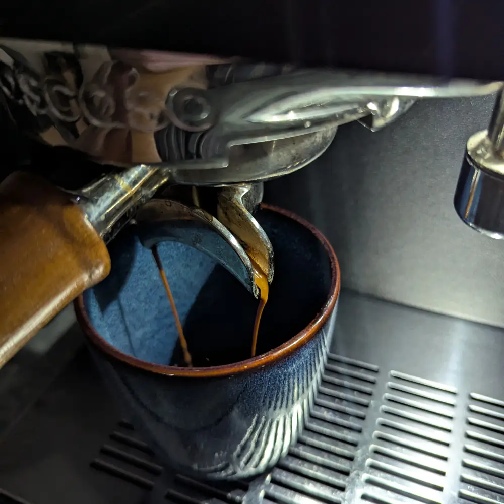 Closeup photo of an #ascaso espresso machine producing the first coffee of the day into a blue ceramic cup