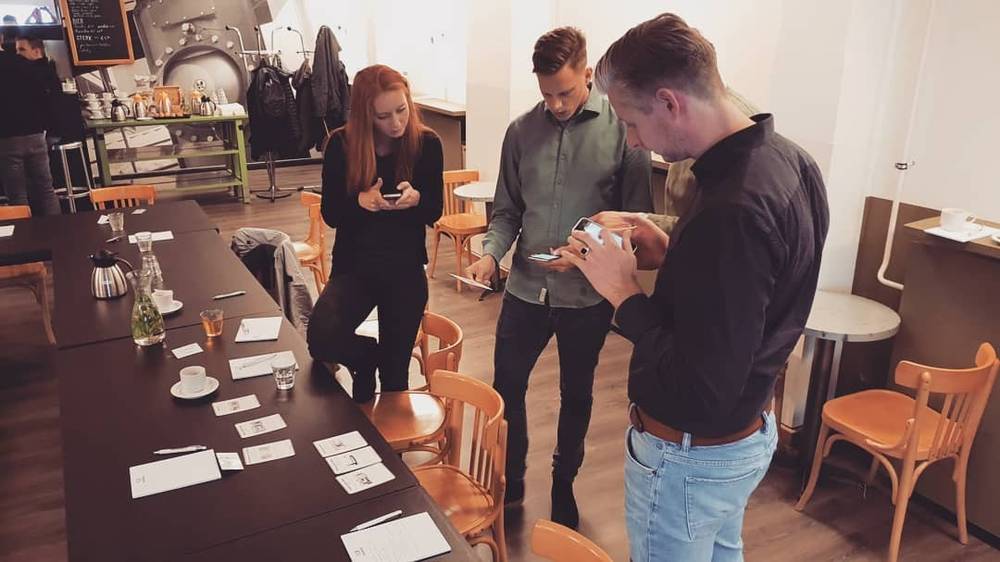 People stand around a table covered with papers and glasses, chatting during a workshop break.